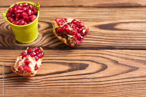 Two halves of fresh ripe red pomegranate with seeds near full green metal bucket of seeds on old brown weathered rustic wooden table