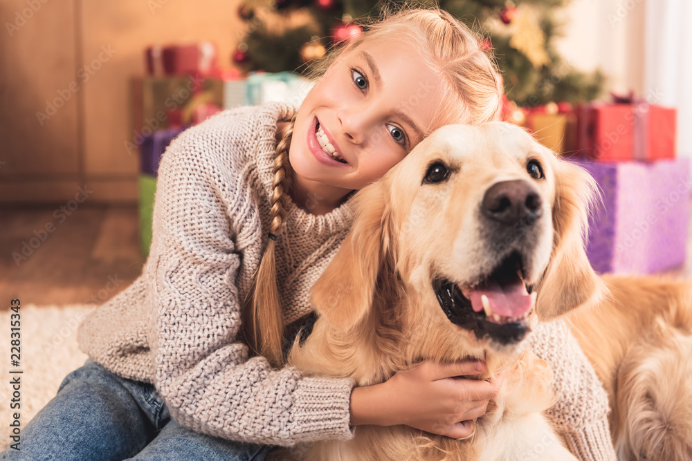 smiling kid hugging golden retriever dog and sitting near christmas tree smiling kid hugging golden retriever dog and sitting near christmas tree