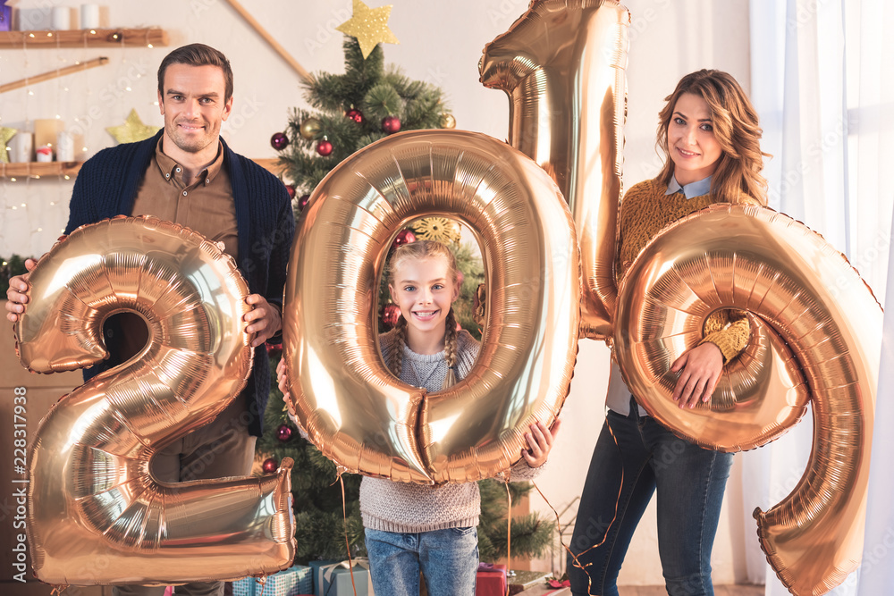 smiling family holding 2019 new year golden balloons at home with christmas tree