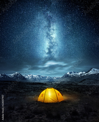 Camping in the wilderness. A pitched tent under the glowing  night sky stars of the milky way with snowy mountains in the background. Nature landscape photo composite. © James Thew