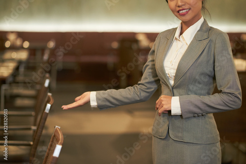 Crop elegant woman in suit making welcoming gesture inviting to visit restaurant in hotel