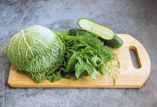 Green vegetables cabbage, fresh cucumbers, dill, basil on a wooden board on a dark background. The concept of vegan cuisine, diet food, detox. Green vegetables on a dark background.