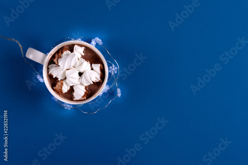 Hot chocolate with marshmallow candies decorated illumination light on blue paper background. Top view. Copy space