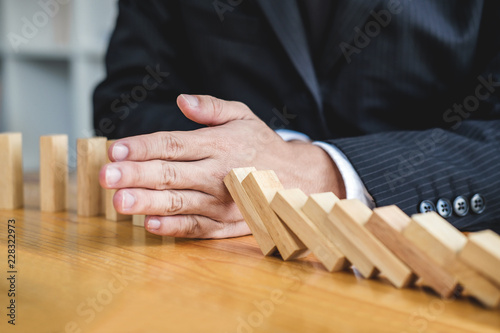 Wooden game strategy, Businessman hand stopping falling wooden dominoes effect from continuous toppled or risk, strategy and successful intervention concept for business