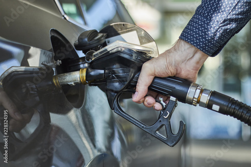 Closeup of a hand filling a fuel tank of a car with fuel dispenser in petrol station.