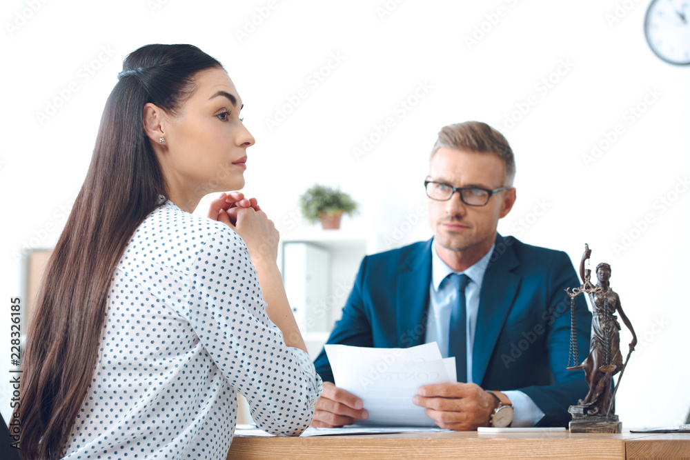 lawyer holding papers and looking at young upset woman in office lawyer holding papers and looking at young upset woman in office