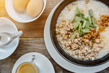 ฺBreakfast Rice porridge with pork chops and seasoning in black bowls and coffee cup on top view wood table, Chinese food.