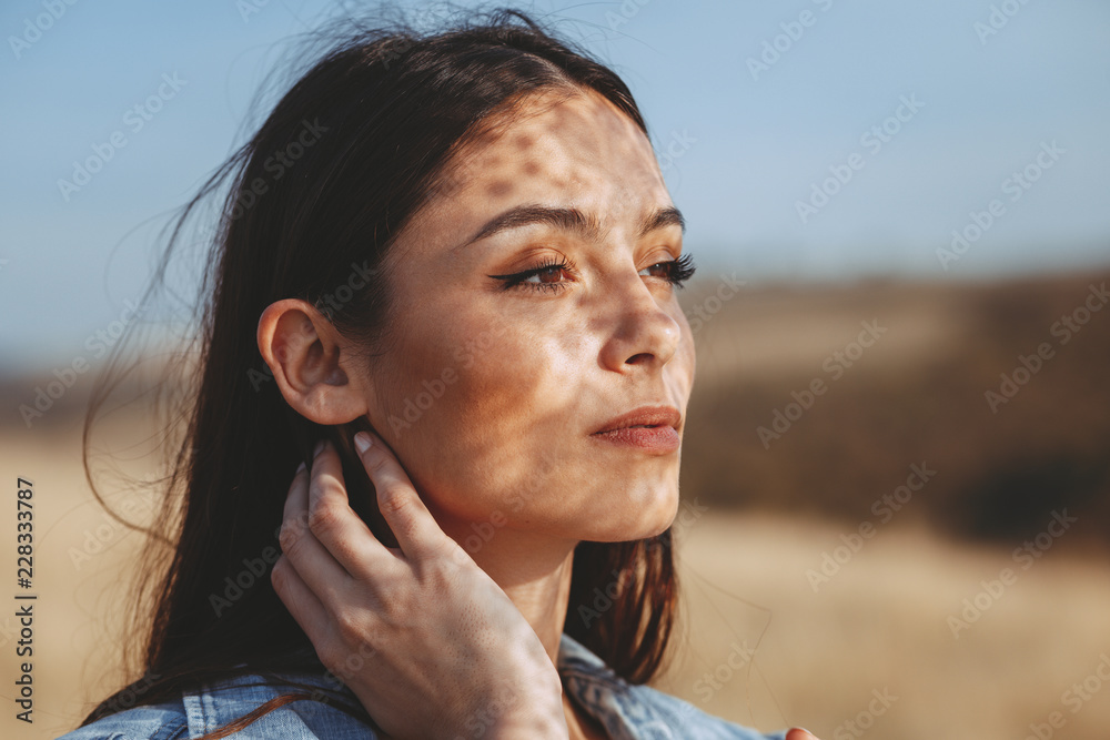 Fototapeta premium Portrait of a young woman with shadows texture on the face in a meadow with
