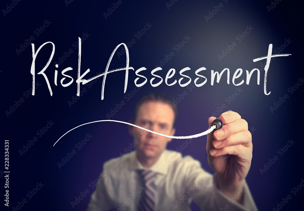 A businessman writing a Risk Assessment concept with a white pen on a clear screen.