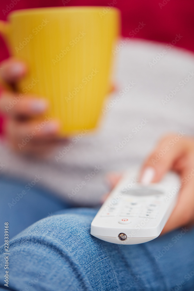 Girl holding TV remote and drinking coffee / tea on a couch. Girl holding TV remote and drinking coffee / tea on a couch.