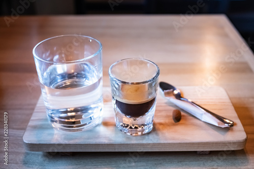 Espresso served in glass on stylish wood plate. Cup of italian coffee and glass of fresh water, front view