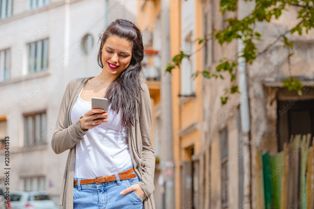 Cute young woman using cellphone in urban surroundings.