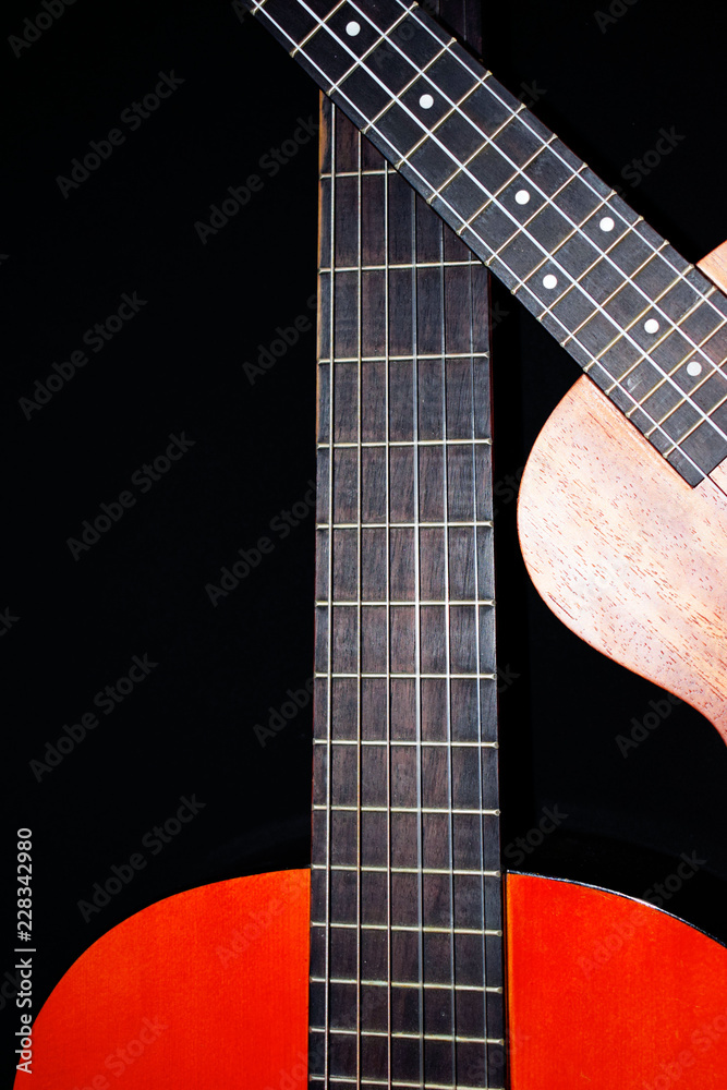 Fototapeta premium Guitar on black background. Musical hobby. The neck of the guitar. Ukulele. Strings. Musical instruments.