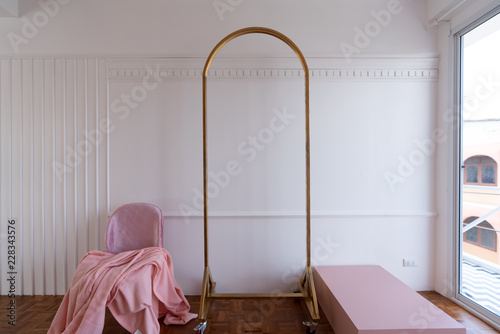 Composition of oldrose blanket setting on mid century modern chair in baby pink color setting in white wooden stripe and classic moulding wall and gold clothes hanger.   photo