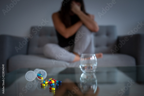 Depressed woman on a couch with medication pills and a glass of water