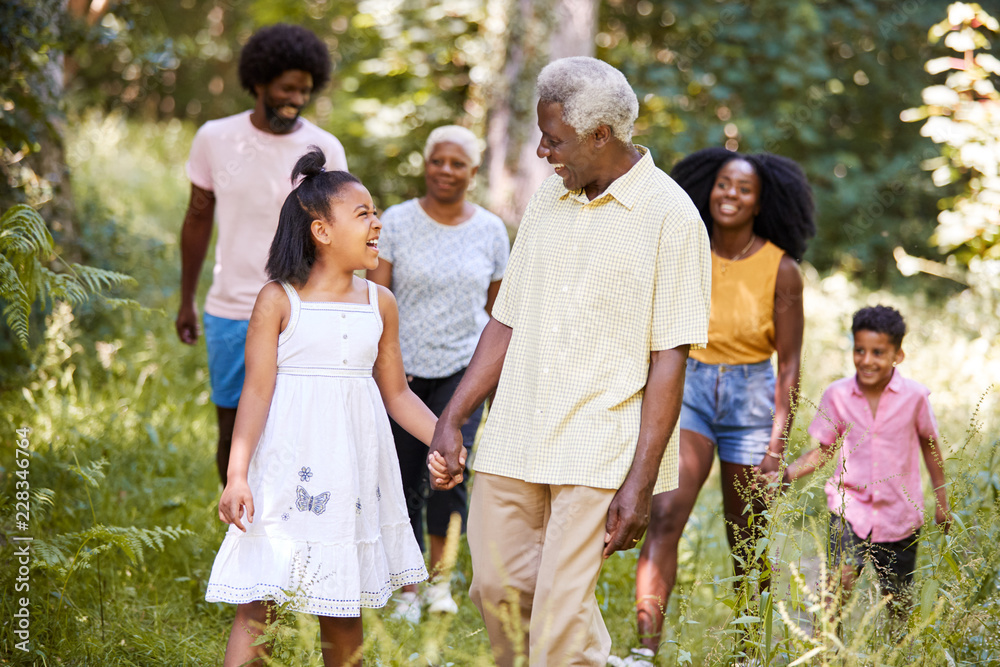 Senior black man and granddaughter walk with family in woods Senior black man and granddaughter walk with family in woods