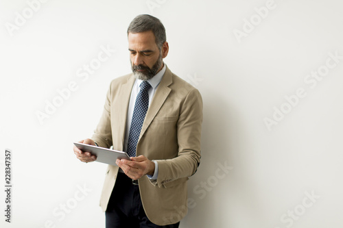 Handsome senior businessman with digital tablet by wall