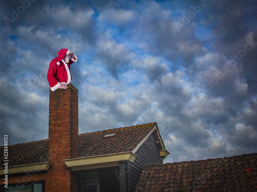 Merry Christmas and happy holidays! Santa Claus sitting in a chimney and looking at distance.