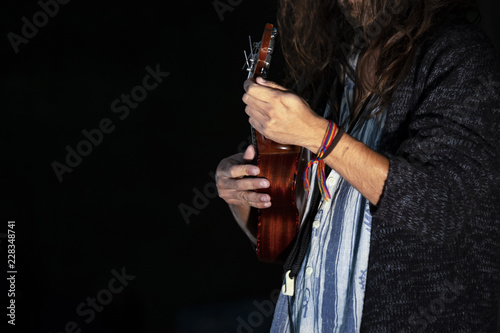 Musician with long hair on stage does a performance playing a small ukulele.