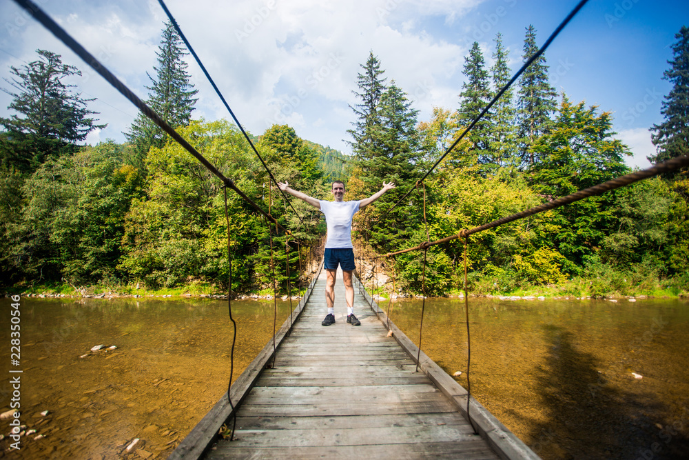 Fototapeta premium Tourist man walk by long wooden suspension bridge above river. balance concept