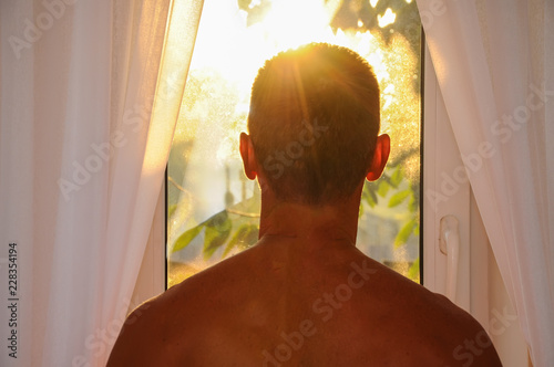 man looks out the window for the morning sunrise