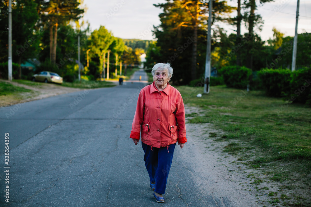 Obraz premium Elderly woman walking down the street in village.