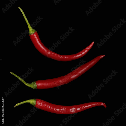 three red chili peppers isolated on black background