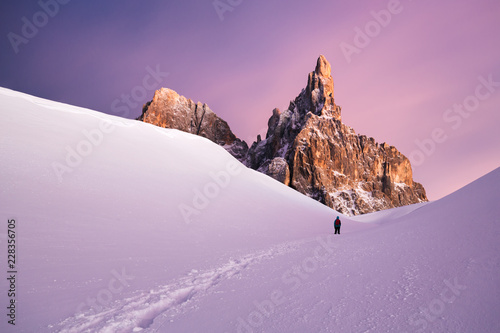 Man walking through snow covered path with mountains in the background