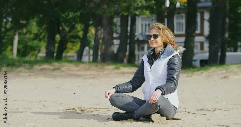 Girl in sunglasses sits on seaside in cold autumn Girl in sunglasses sits on seaside in cold autumn