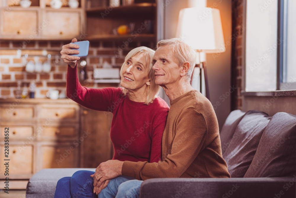 Obraz premium Selfie time. Inspired aged spouses sitting together and taking selfies at home