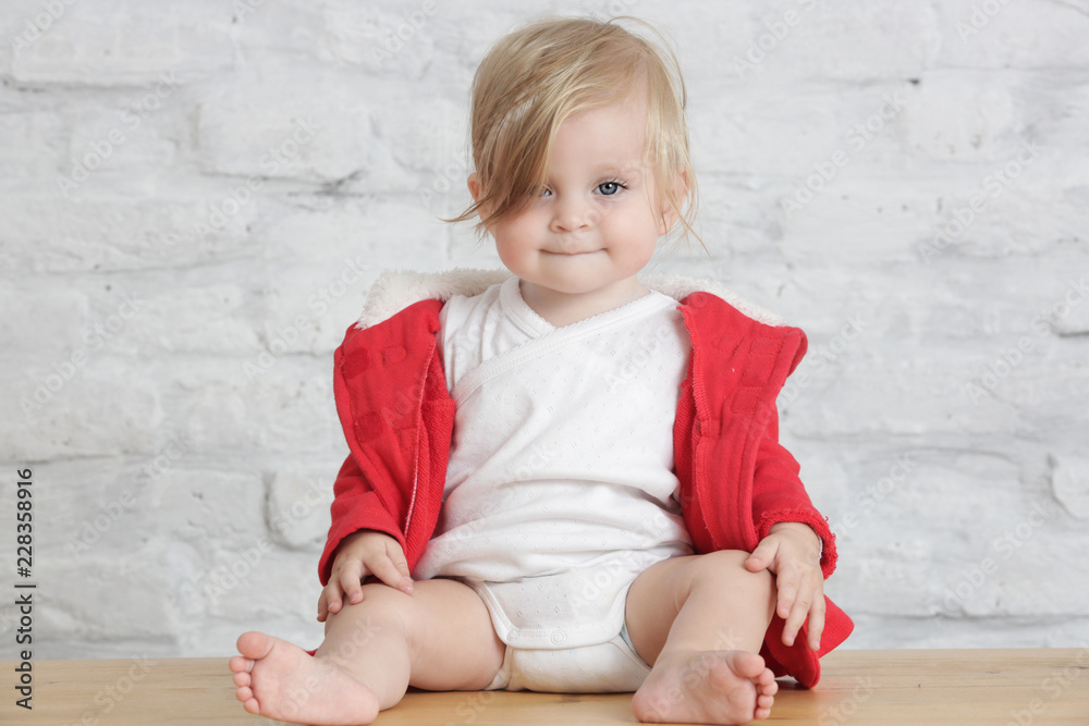 Fototapeta premium Indoor portrait of a cute blond baby in the red and white outfit 