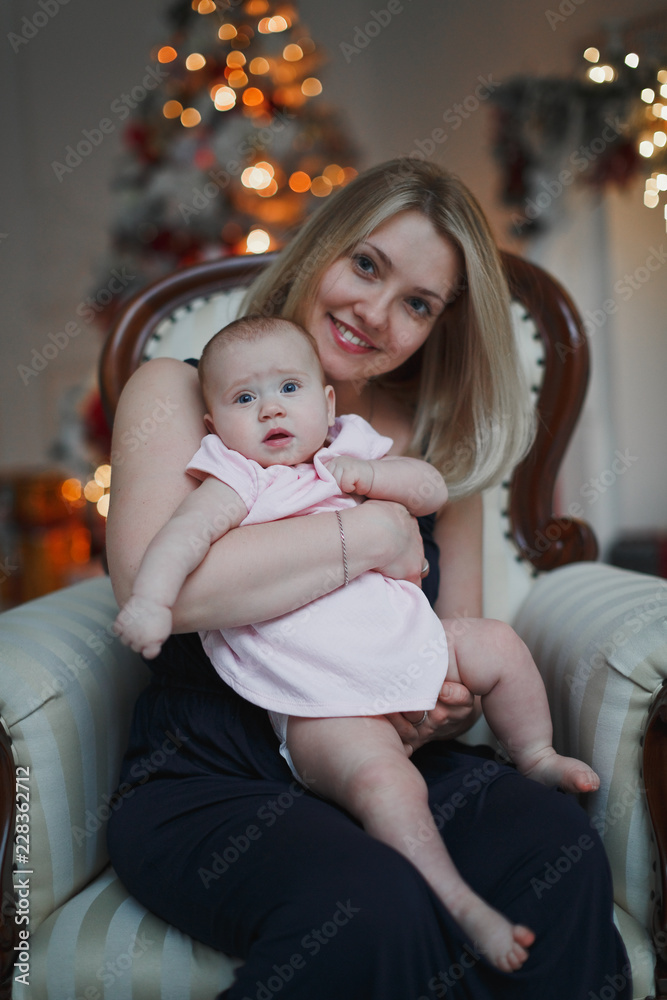 Happy young smiling mother hugging baby daughter for the Christmas tree lights in the background. Family, motherhood and holidays concept. Happy young smiling mother hugging baby daughter for the Christmas tree lights in the background. Family, motherhood and holidays concept.