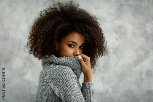 Portrait of young african american woman with an afro hair wear high-neck wool and cashmere sweater, hiding her mouth under the golf