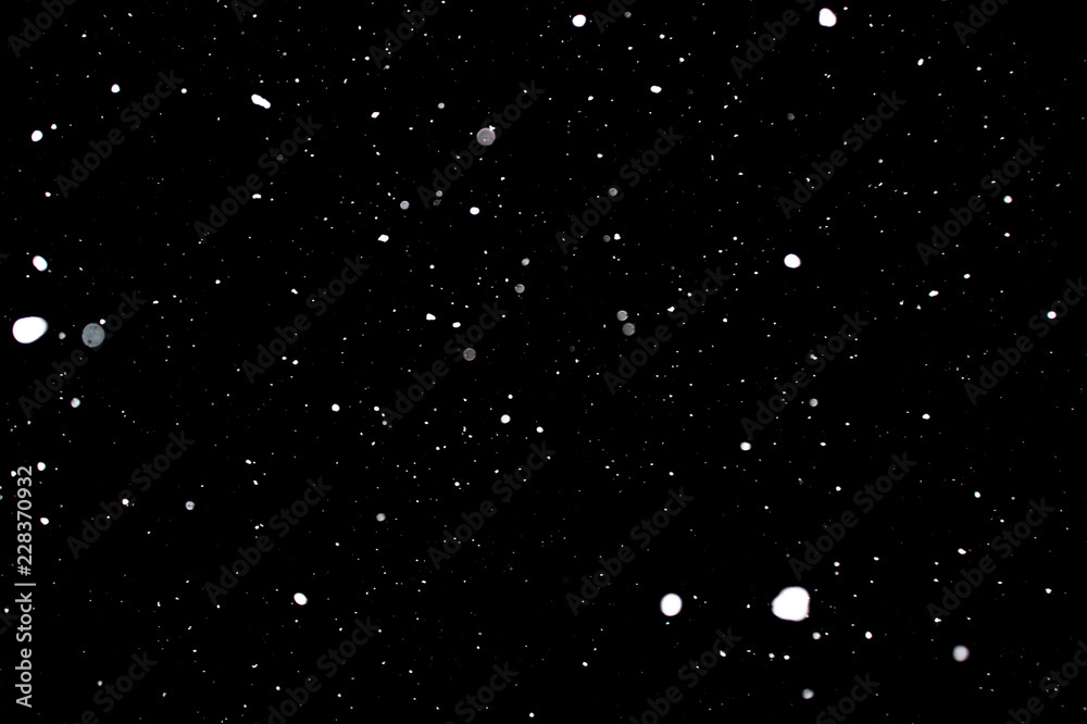 Snowstorm texture. Bokeh lights on black background, shot of flying snowflakes in the air