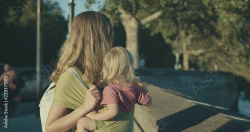 Mother with toddler in sling standing by river in city