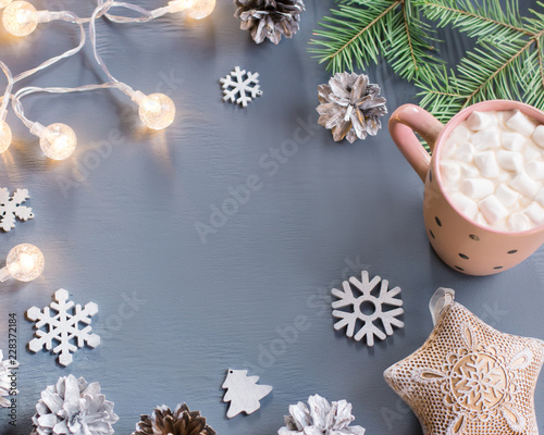 Winter background with hot drink with marshmallows, Christmas lights, fir tree and decorations.