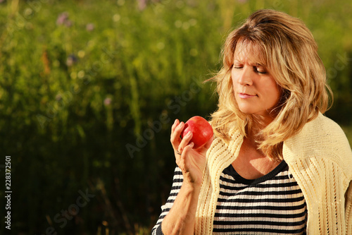 Happy mature woman regarding an apple in the grass outdoor