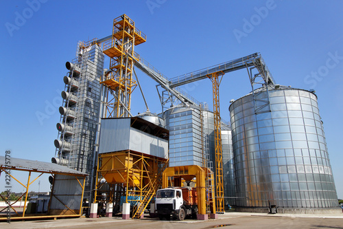 Agricultural silo truck of orange color on the territory of grain storage in sunny weather.