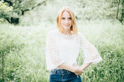 Beautiful attractive young woman posing in spring park wearing white knitted top and blue jeans, modern creative toning