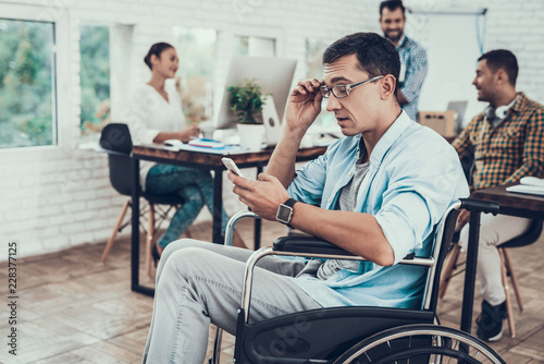 Man in Glasses on Wheelchair with Phone in Office.