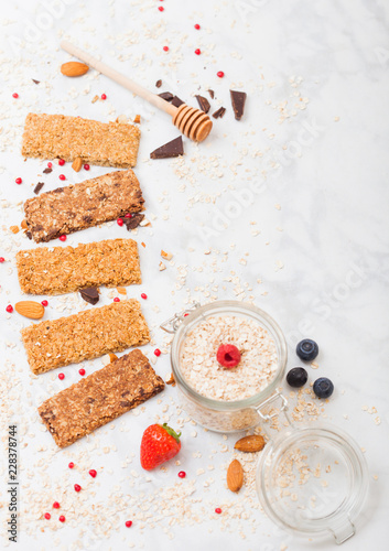 Organic cereal granola bar with berries with honey spoon and jar of oats on marble background. Top view. Strawberry, raspberry and blueberry with almond nuts. photo