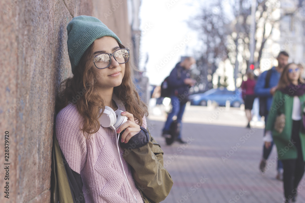 Cute teen girl in a hat and headphones on a city street. Young stylish woman outdoor.