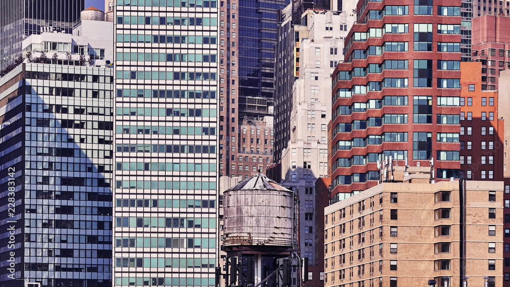 Water tank among modern buildings in Manhattan, retro cinematic toning applied, New York, USA.