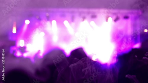 Blurred scene of a rock concert with musicians on stage and the crowd in the shadow. Purple lighting effects. A purple smoke covers the screen.