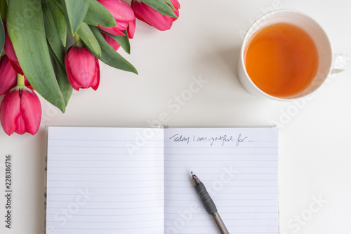 Close up high angle view of red tulips, cup of tea and journal with pen and handwritten "Today I am grateful for"