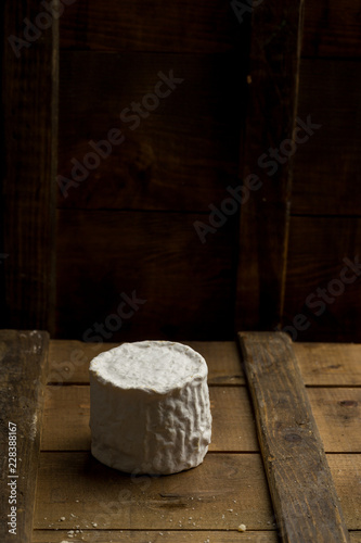 Whole head of brie cheese on wooden board on dark background