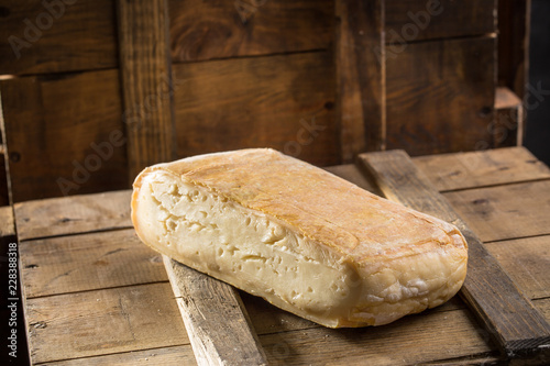 Piece of taleggio cheese on wooden board on dark background
