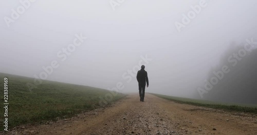 Back view of a person walks on foggy countryside road.