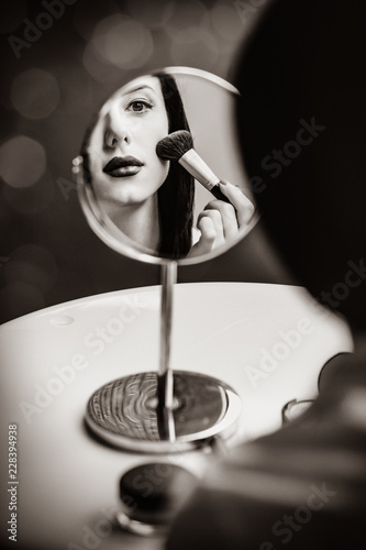 portrait of the beautiful young woman doing her make-up and looking in the mirror