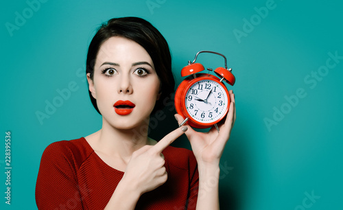 Portrait of young surprised woman with alarm clock on green background